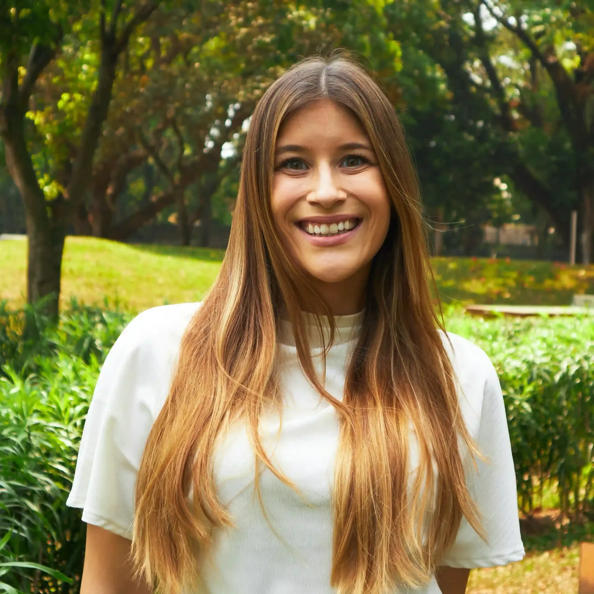 A woman in a brown shirt is smiling in front of a building.