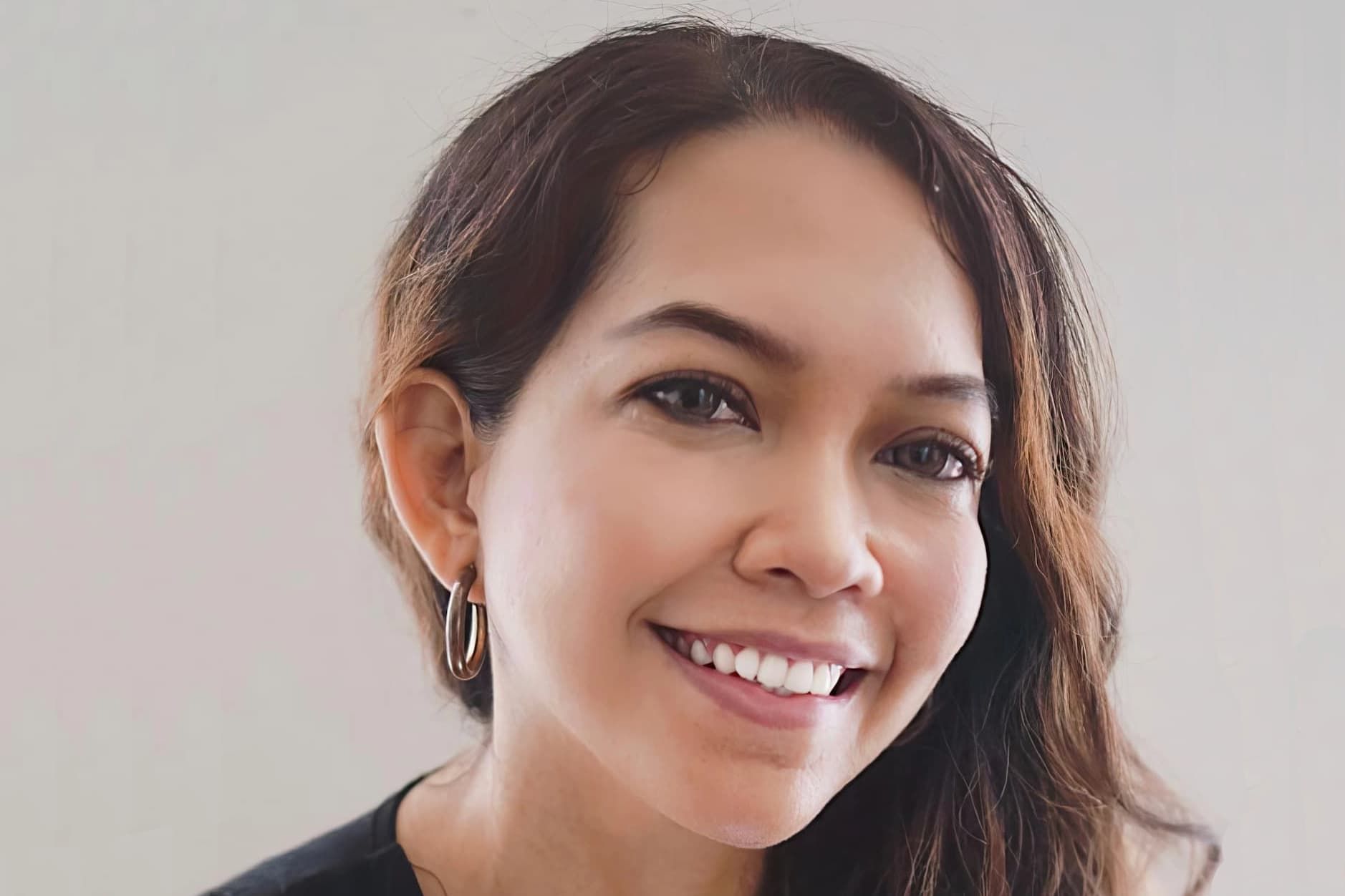 A close up of a woman 's face smiling and wearing earrings.