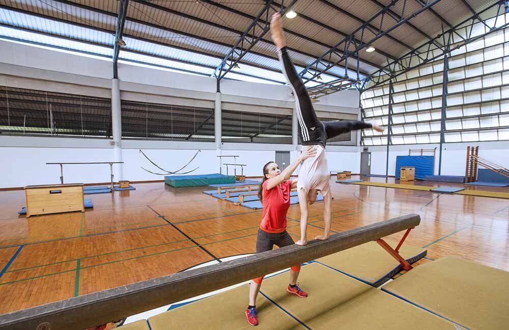 A female gymnast is doing a handstand on a balance beam in a gym.