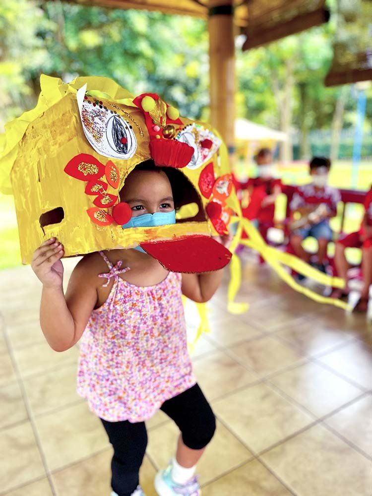 A little girl is wearing a mask and holding a cardboard dragon head.