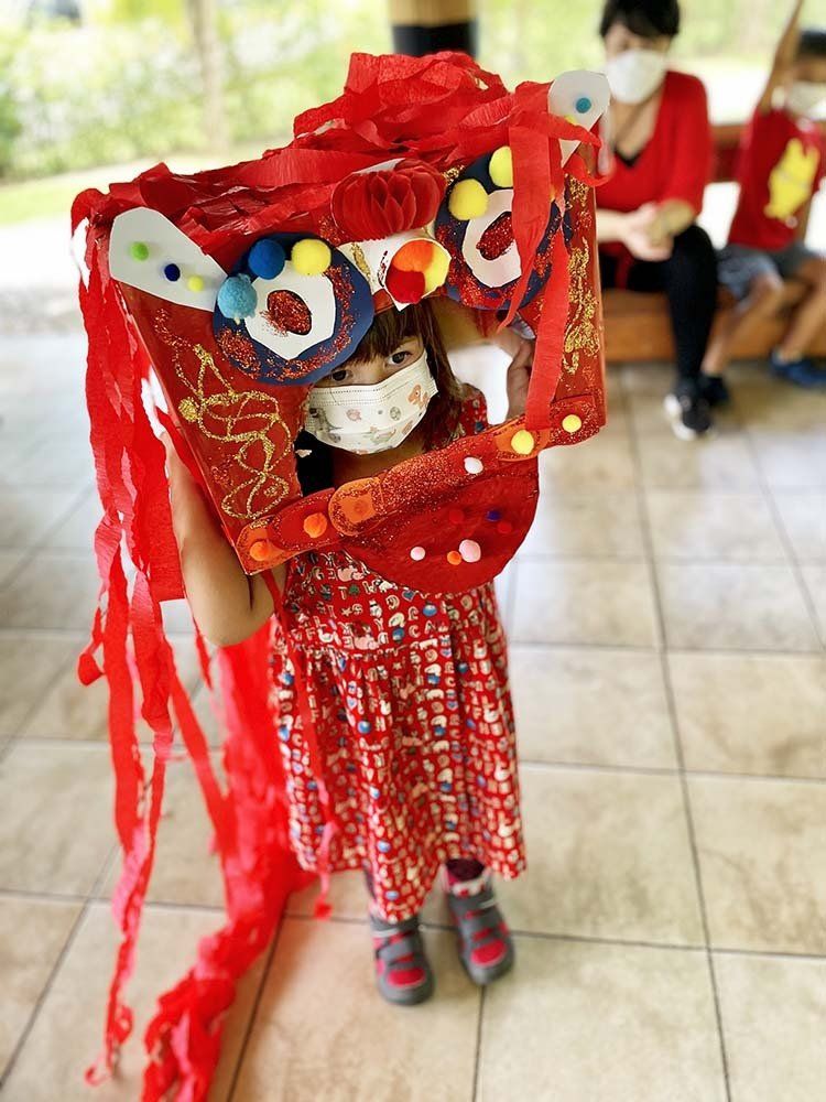 A little girl is wearing a mask and holding a red kite.