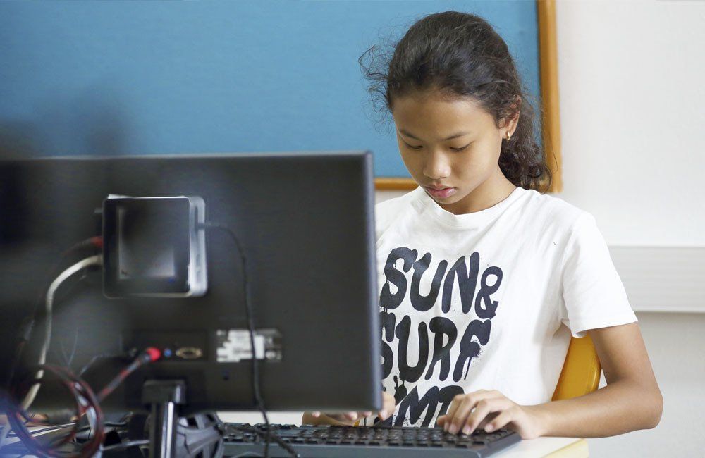 A young girl wearing a shirt that says sung surf is using a computer.