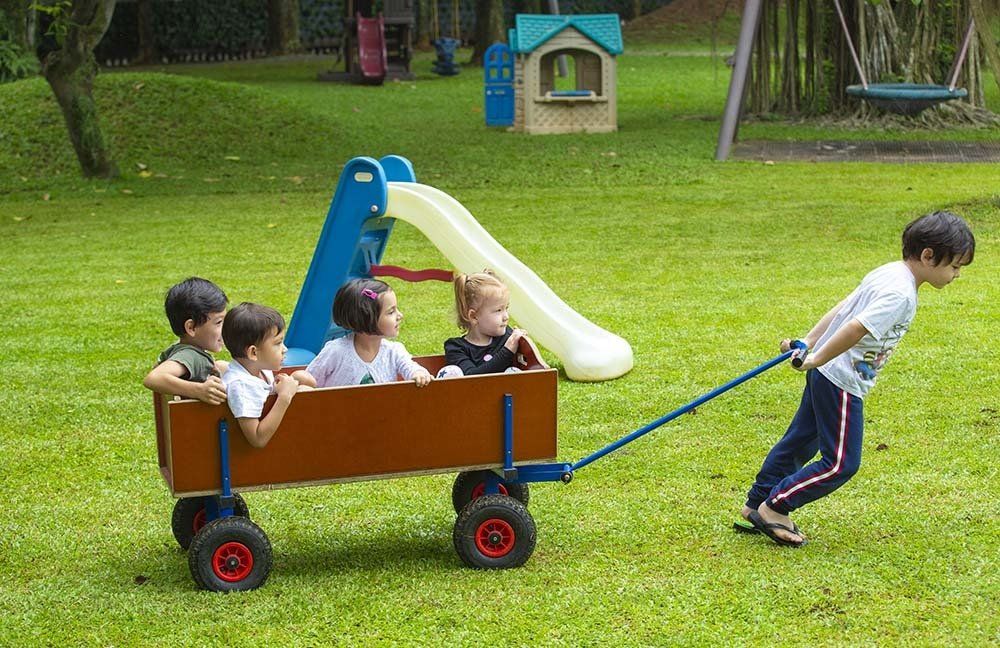 A boy is pulling a wooden wagon with four children in it.