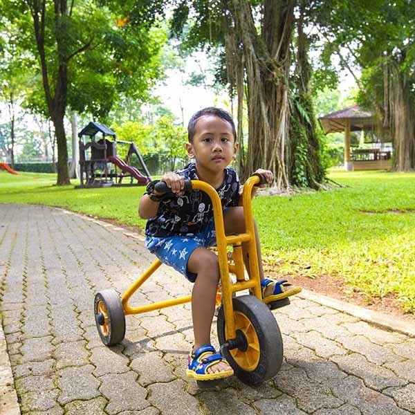 A young boy is riding a yellow tricycle in a park