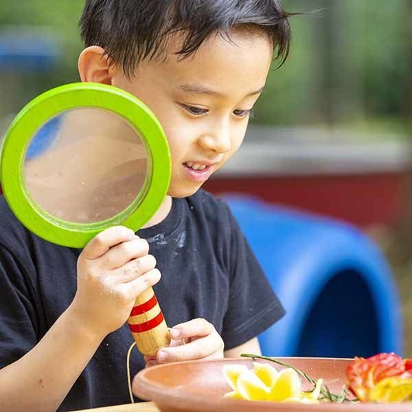 A young boy is looking through a magnifying glass at a bowl of food