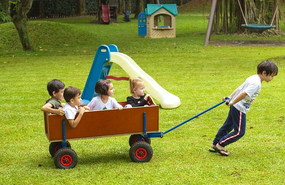 A boy is pulling a wooden wagon with four children in it.