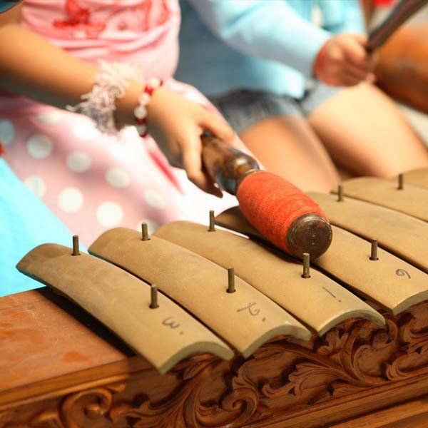 A person is playing a wooden xylophone with a red stick