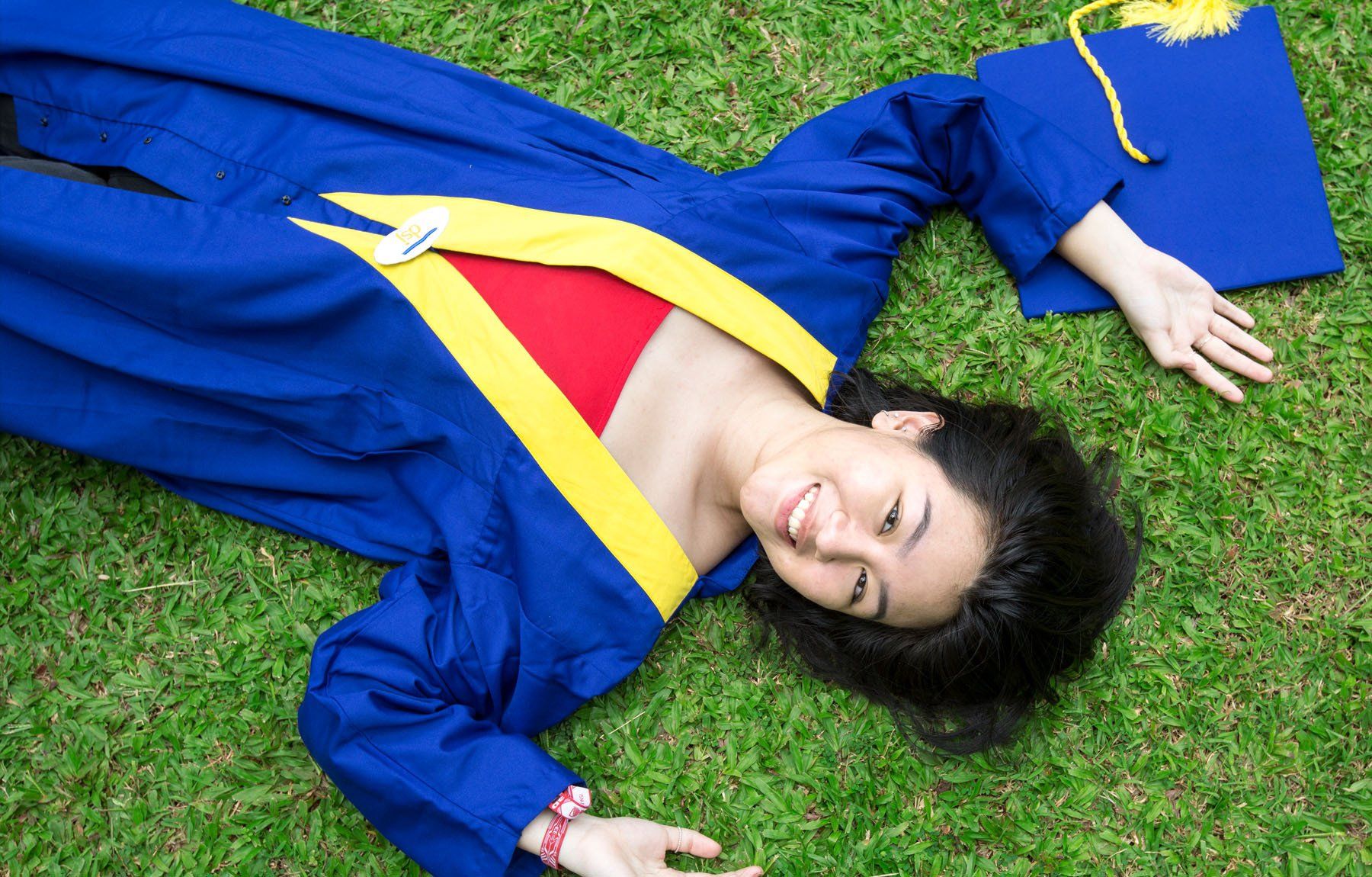A woman in a graduation cap and gown is laying on the grass.