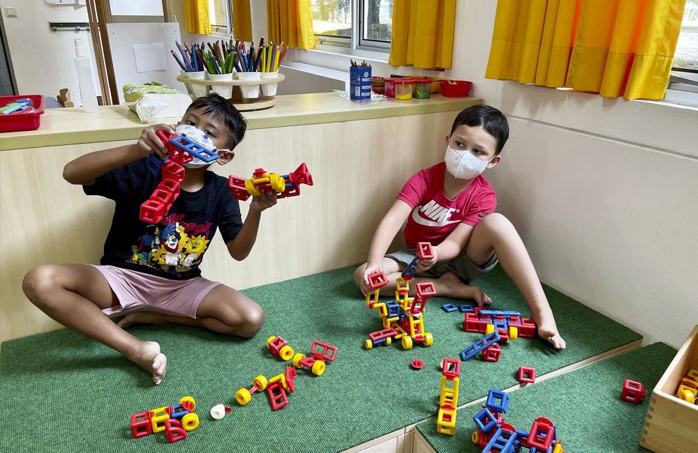 Two young boys wearing face masks are sitting on the floor playing with toys.