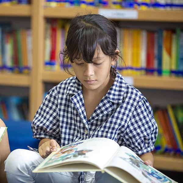 A young girl is sitting on the floor reading a book in a library.
