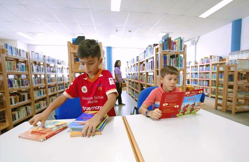 Two young boys are reading books in a library.