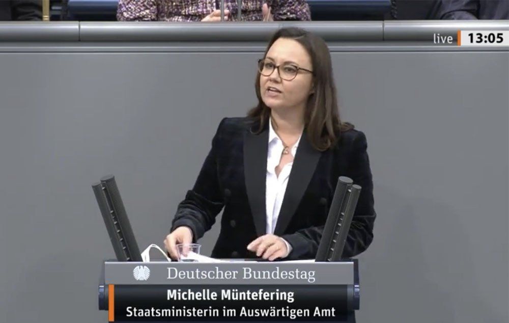 A woman in a suit is giving a speech at a podium.