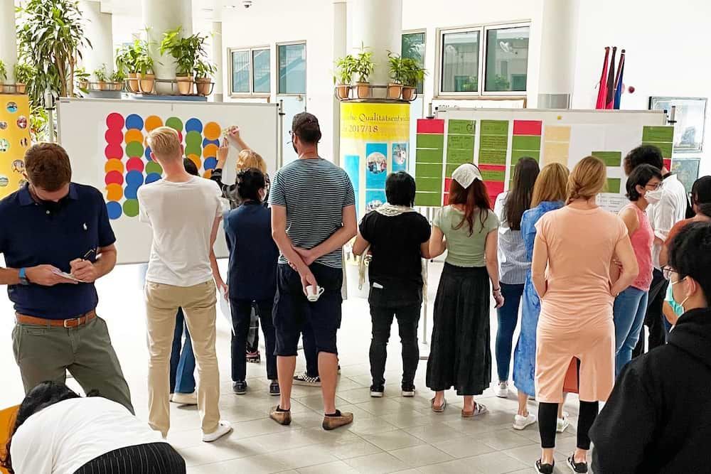 A group of people are standing in a room looking at a whiteboard.