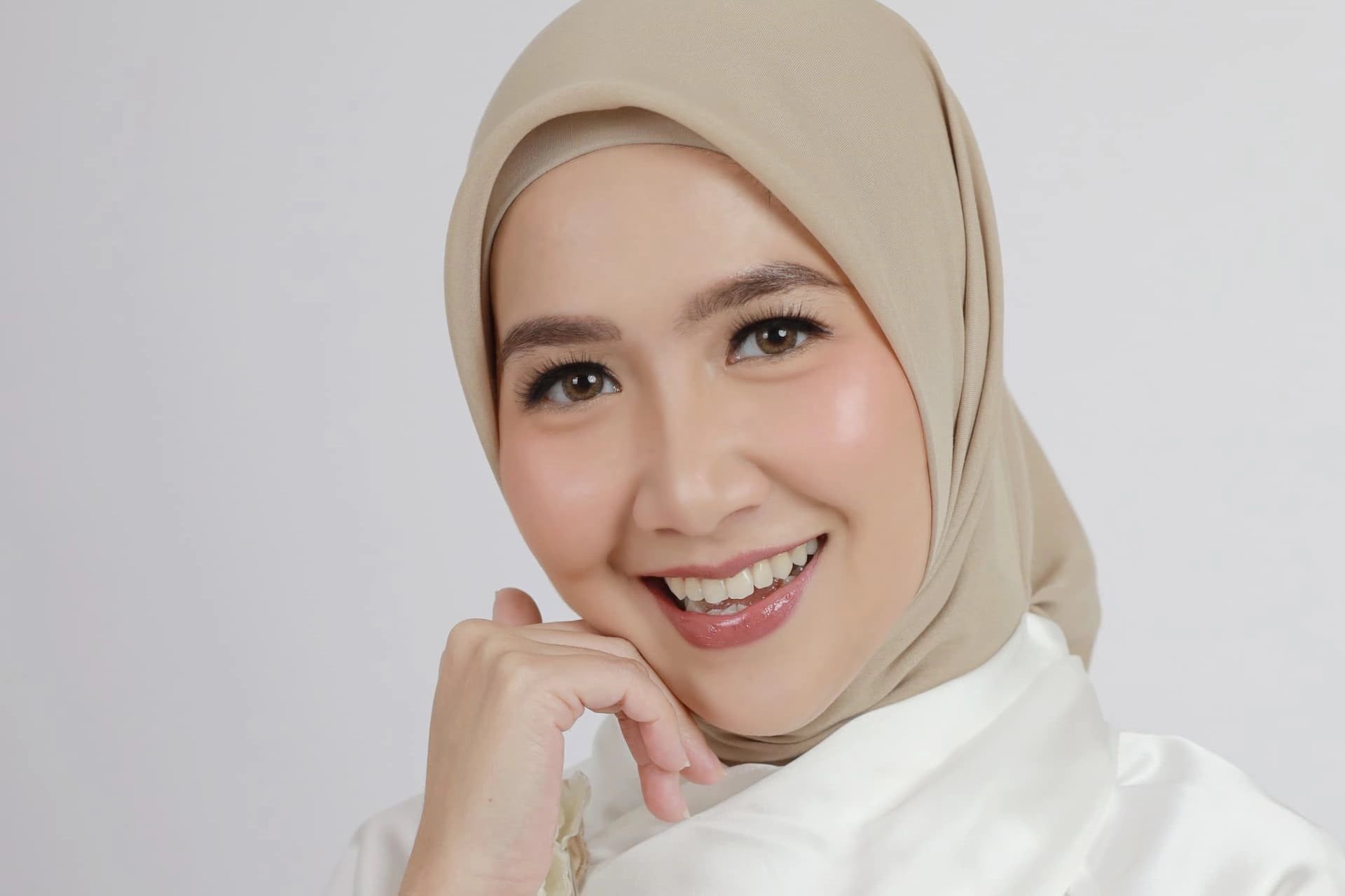 A woman wearing a hijab and a white shirt is smiling.