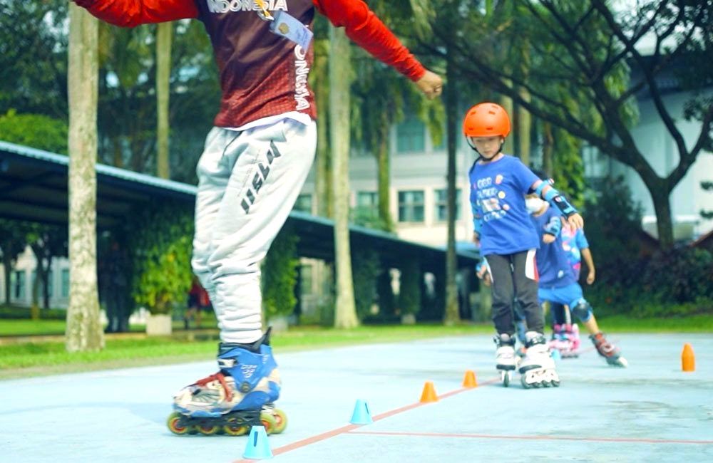 Child dressed in traditional martial arts attire practicing Silat in an indoor sports hall.