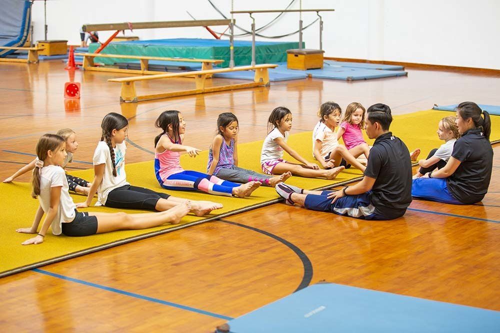 A group of children are sitting on the floor in a gym.