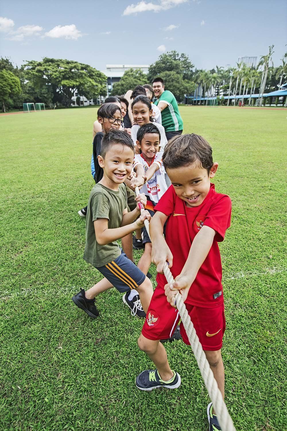 Group of smiling children playing tug-of-war on a grassy field, pulling the rope with determination and teamwork.