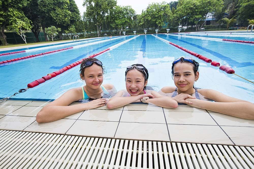 Three girls are sitting on the edge of a swimming pool.