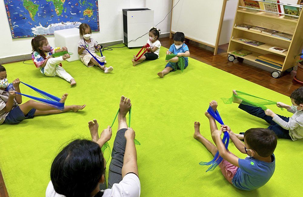 A group of children are sitting on the floor in a circle playing with rubber bands.