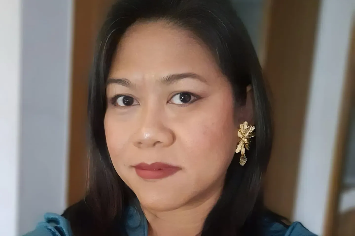 A woman wearing a blue shirt and gold earrings is looking at the camera.
