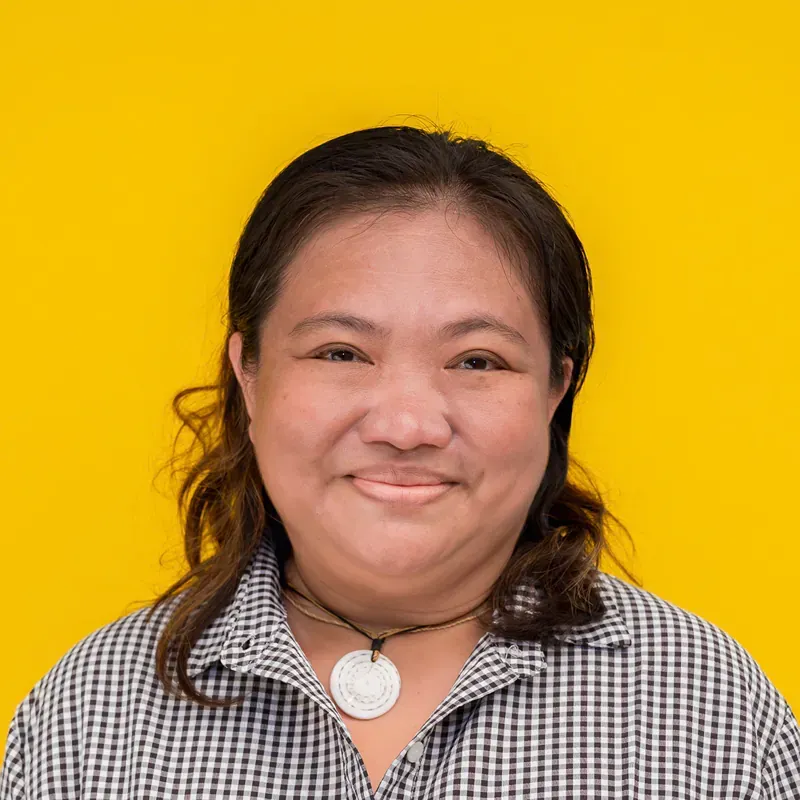 A woman wearing a yellow shirt and a blue necklace is smiling for the camera.