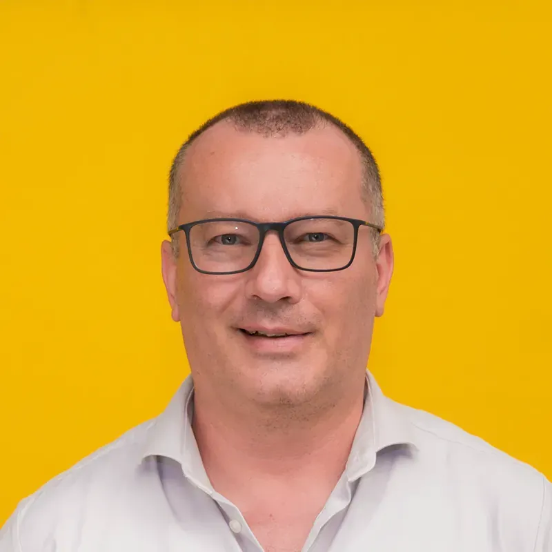 A man wearing glasses and a blue shirt is smiling for the camera.