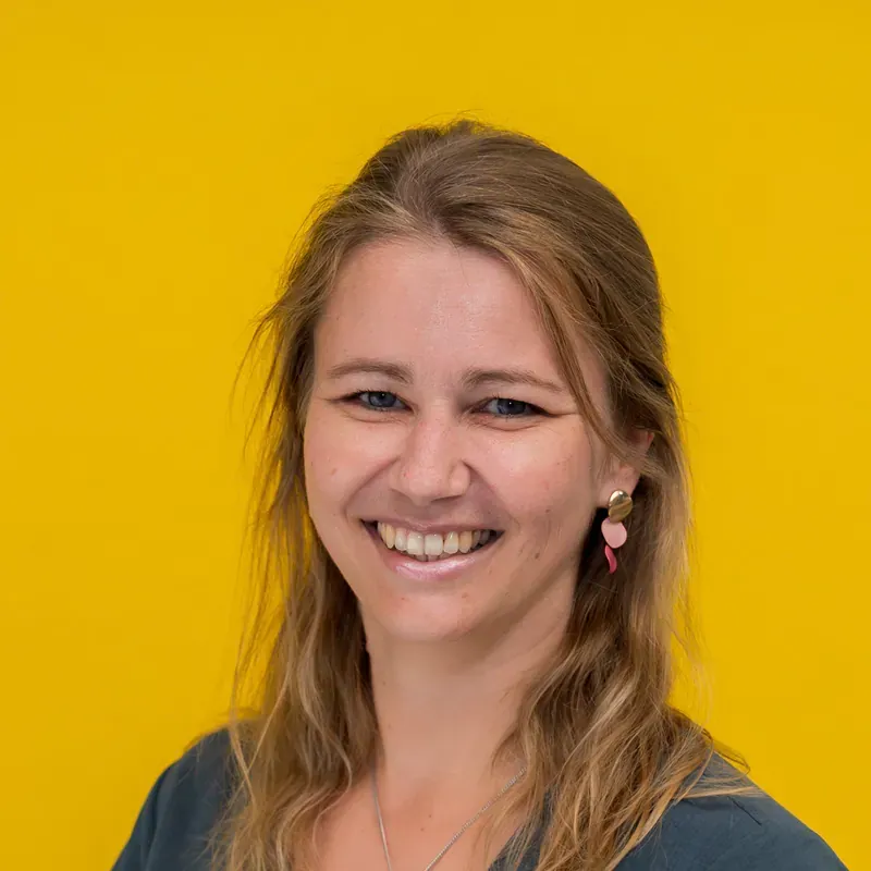 A woman in a striped shirt is standing in front of a white wall.