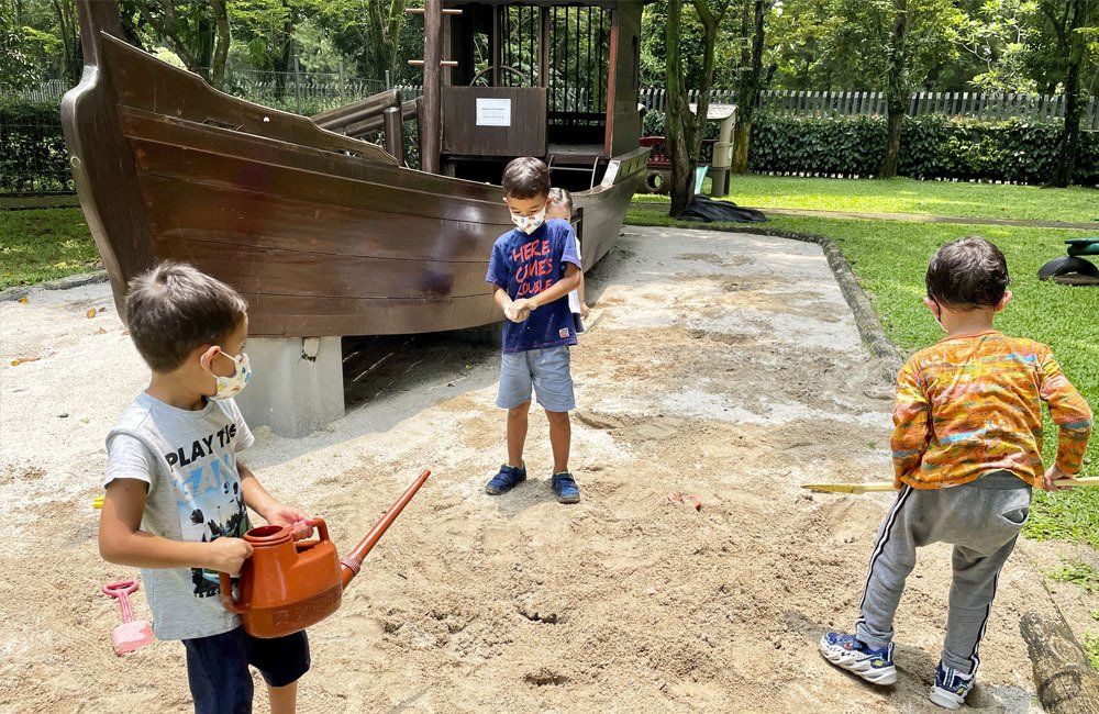 Three young boys are playing in the sand in a park.