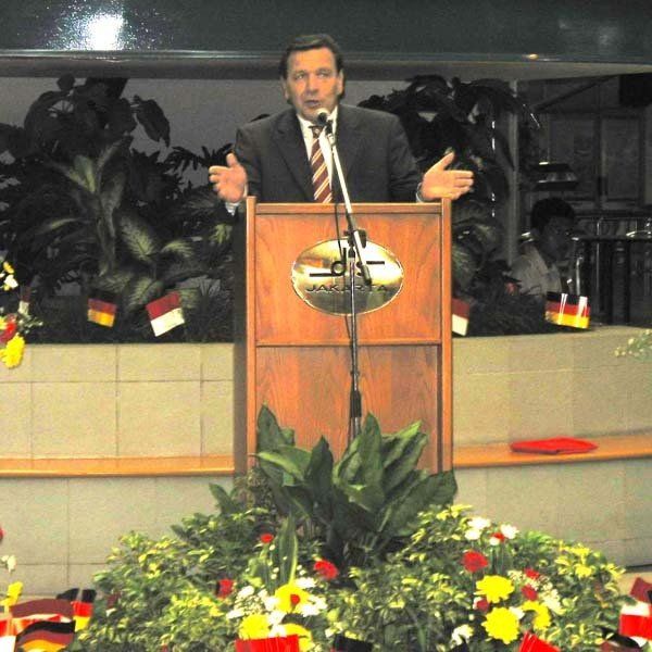 A man in a suit and tie stands at a podium speaking into a microphone