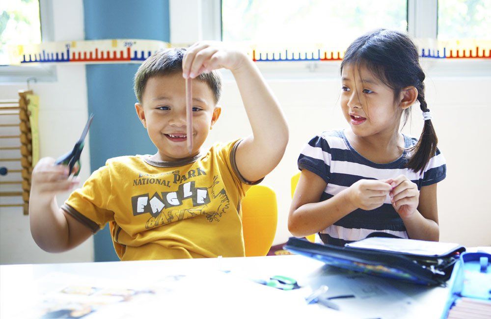 A boy and a girl are sitting at a table playing with scissors.
