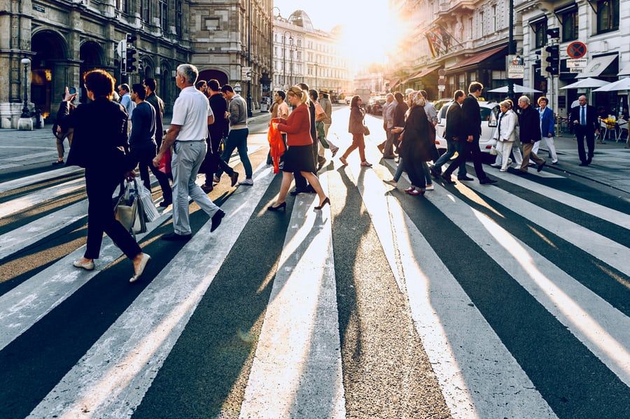 A large group of people are crossing a busy city street.