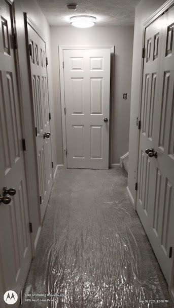 Narrow hallway with white doors on both sides, covered floor, and a closed door at the end.