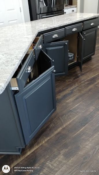 Gray kitchen cabinets with open pull-out drawers and trash bins on a dark wood floor