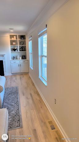 Bright narrow living room with white built-in shelves, wood floors, and a tall window on the right.