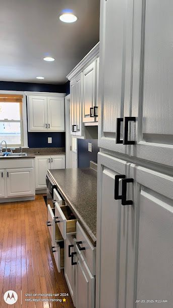 Bright modern kitchen with white cabinets, gray countertops, stainless appliances, and wood floors.