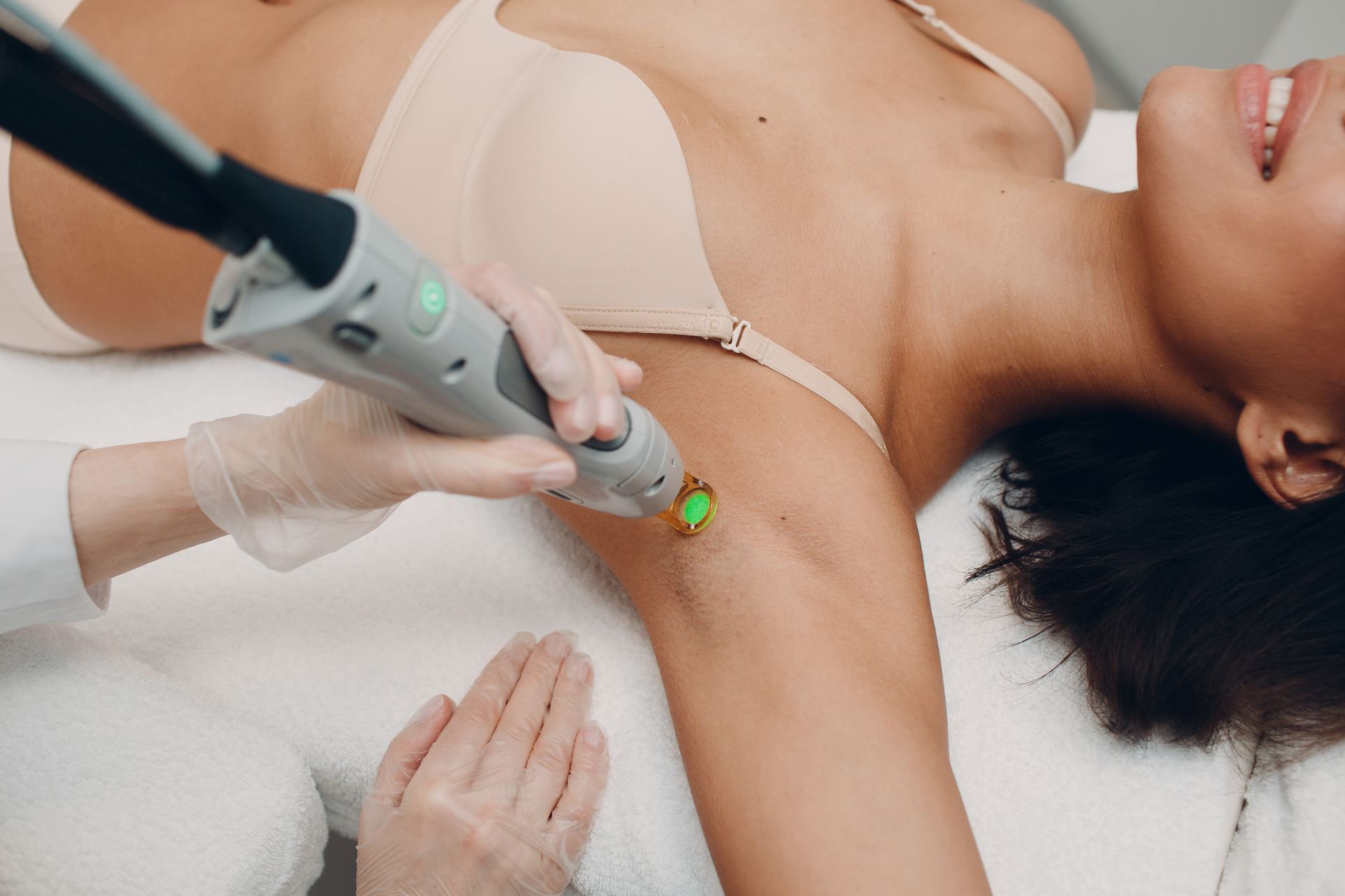 Woman receiving laser hair removal on her underarm; setting is medical, light skin tone, smiling.