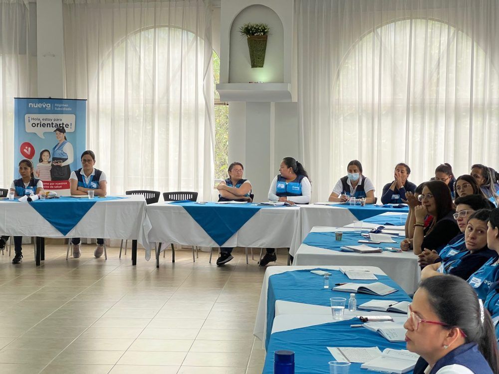 Grupo de mujeres sentadas a la mesa, algunas hablando en una reunión. Decoración azul y blanca.