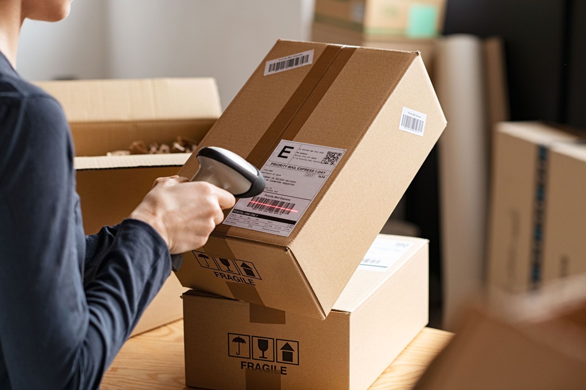 Person scanning a shipping label on a cardboard box with a barcode scanner in a warehouse setting.