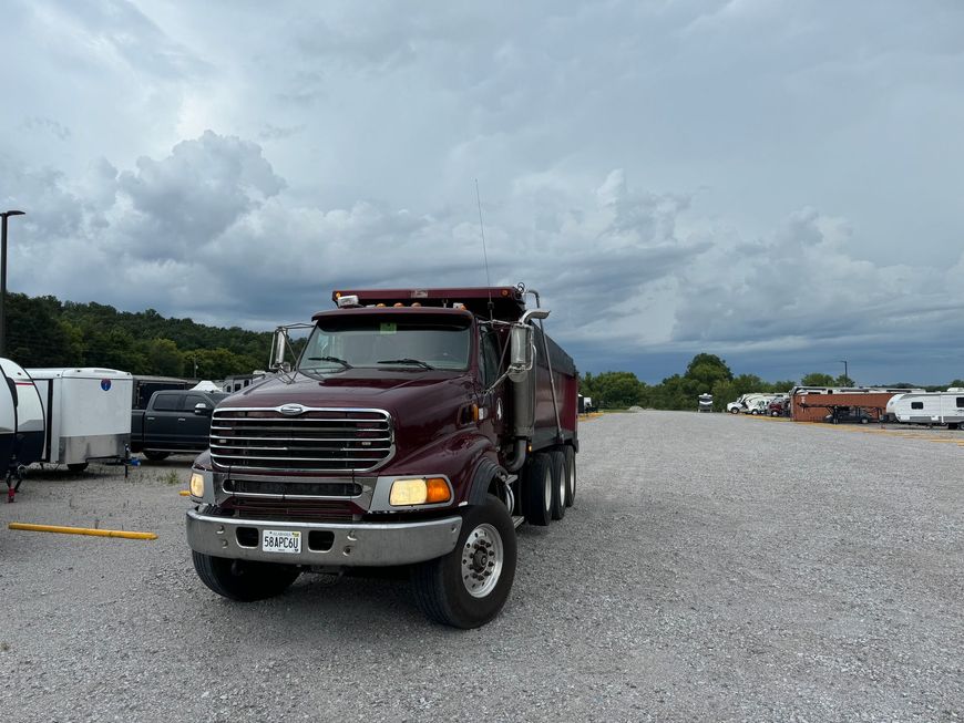 A red dump truck is parked in a gravel lot