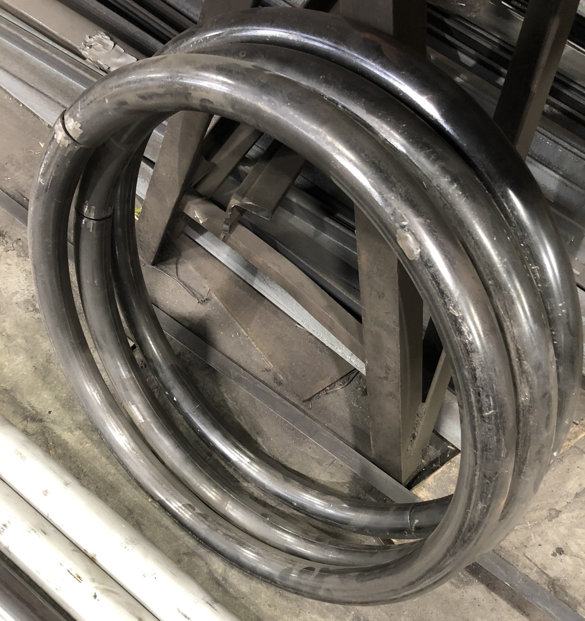 Coiled, welded metal tubing on a metal work surface, reflecting light.