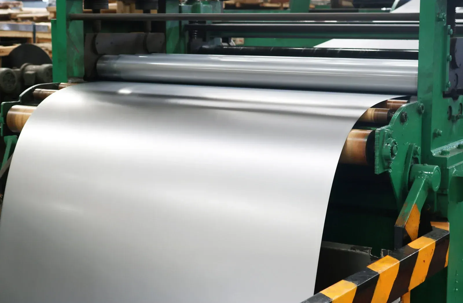 Metal sheet being processed by industrial rollers in a factory.