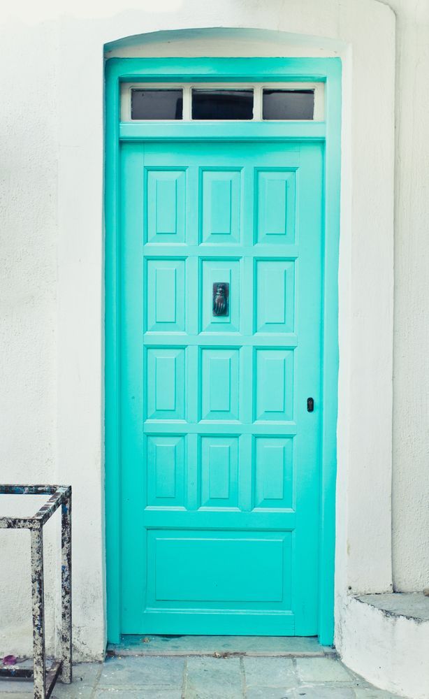 Turquoise door with rectangular panels set in white wall with small window above.