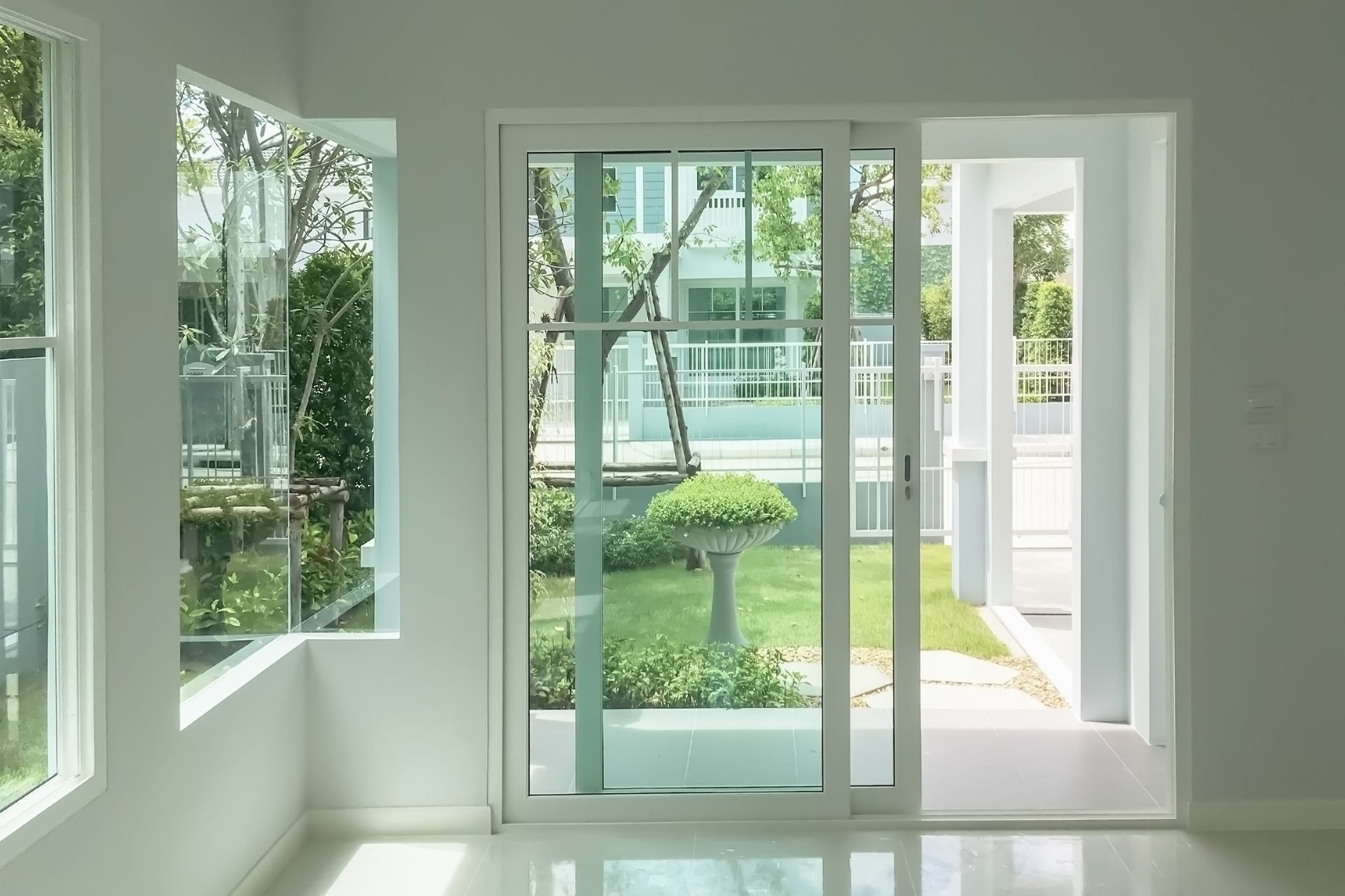 Bright white room interior with glass windows and sliding door leading to a garden.