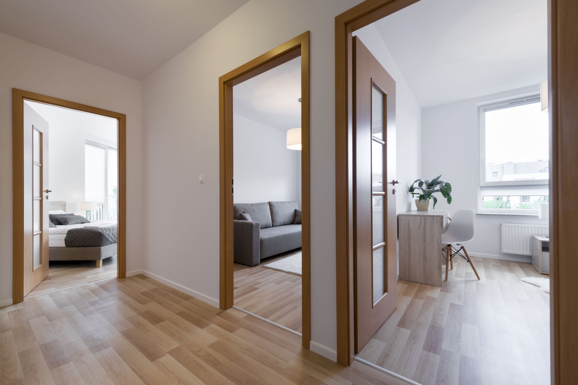 Hallway with three doorways: bedroom, living room, and a third room. Wooden floors and doors, white walls.