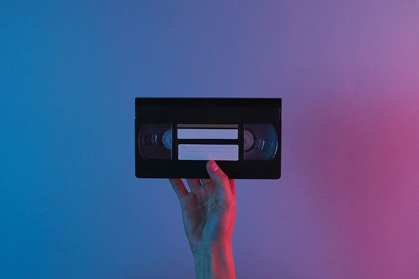 Hand holding a VHS tape against a blue and pink gradient background