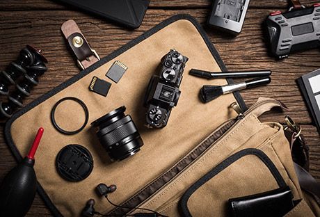 Flat lay of camera gear and accessories on a tan canvas bag over a wooden desk
