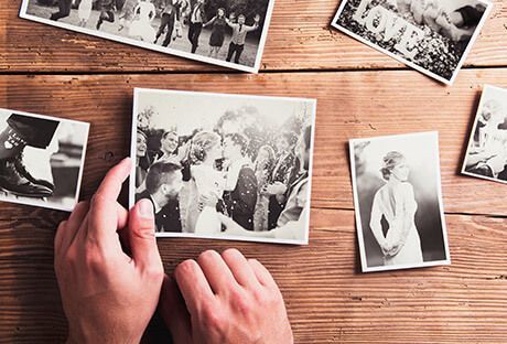 Hands holding a black-and-white photo over a wooden table with scattered old photographs