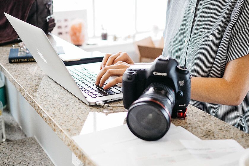 Person typing on a laptop beside a Canon camera on a granite countertop.