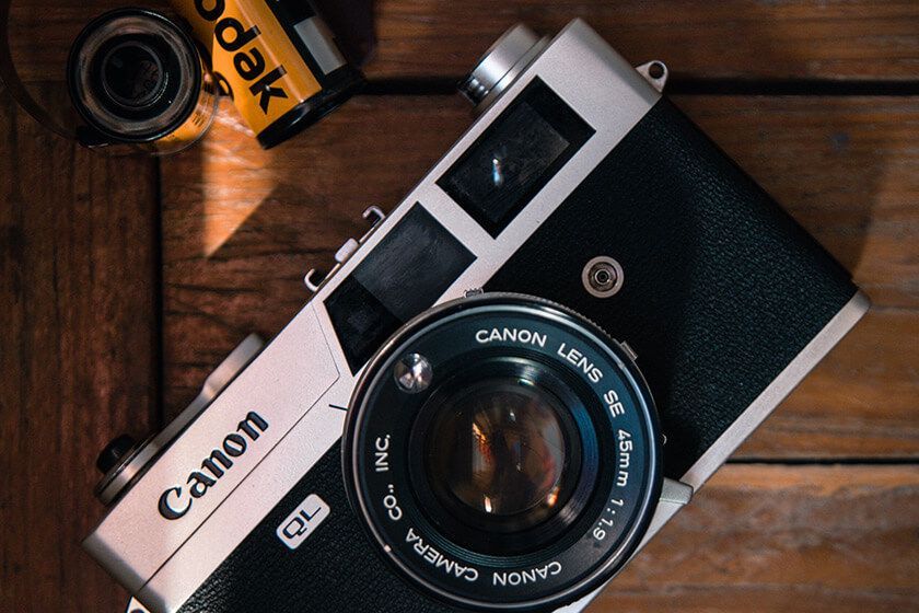 Canon film camera on a wooden table with a Kodak film roll and exposed lens