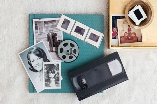 Vintage photo prints and film reel on a turquoise book, with a VHS tape and cassette on a beige surface